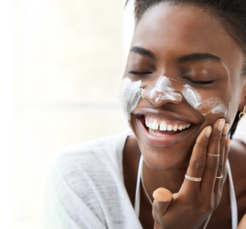 Smiling woman applying moisturizing face cream for healthy glowing skin.